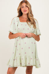 woman wearing a light green maternity dress with floral embroidery and a smocked bodice, styled with flutter sleeves