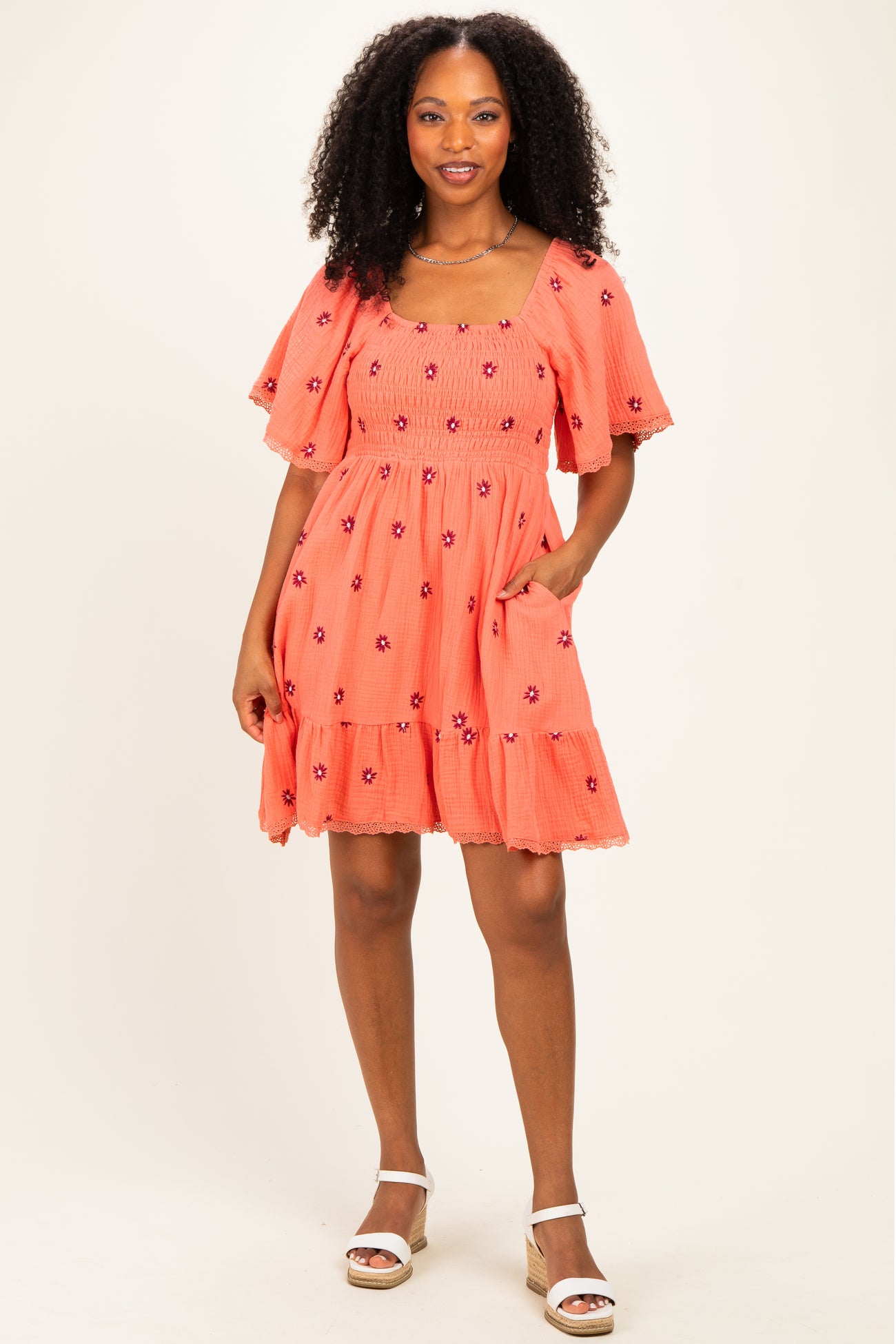 woman wearing an orange short sleeve floral embroidered dress with a square neckline and pockets