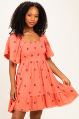 woman wearing a coral embroidered short sleeve dress with a ruffled hem and floral details