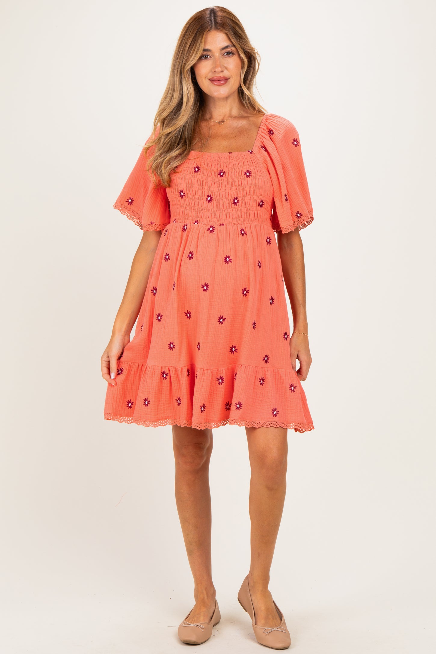 woman wearing a coral maternity dress with floral embroidery and short sleeves