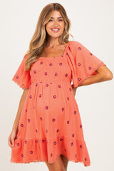woman wearing a coral maternity dress with floral embroidery and flutter sleeves, showcasing her baby bump