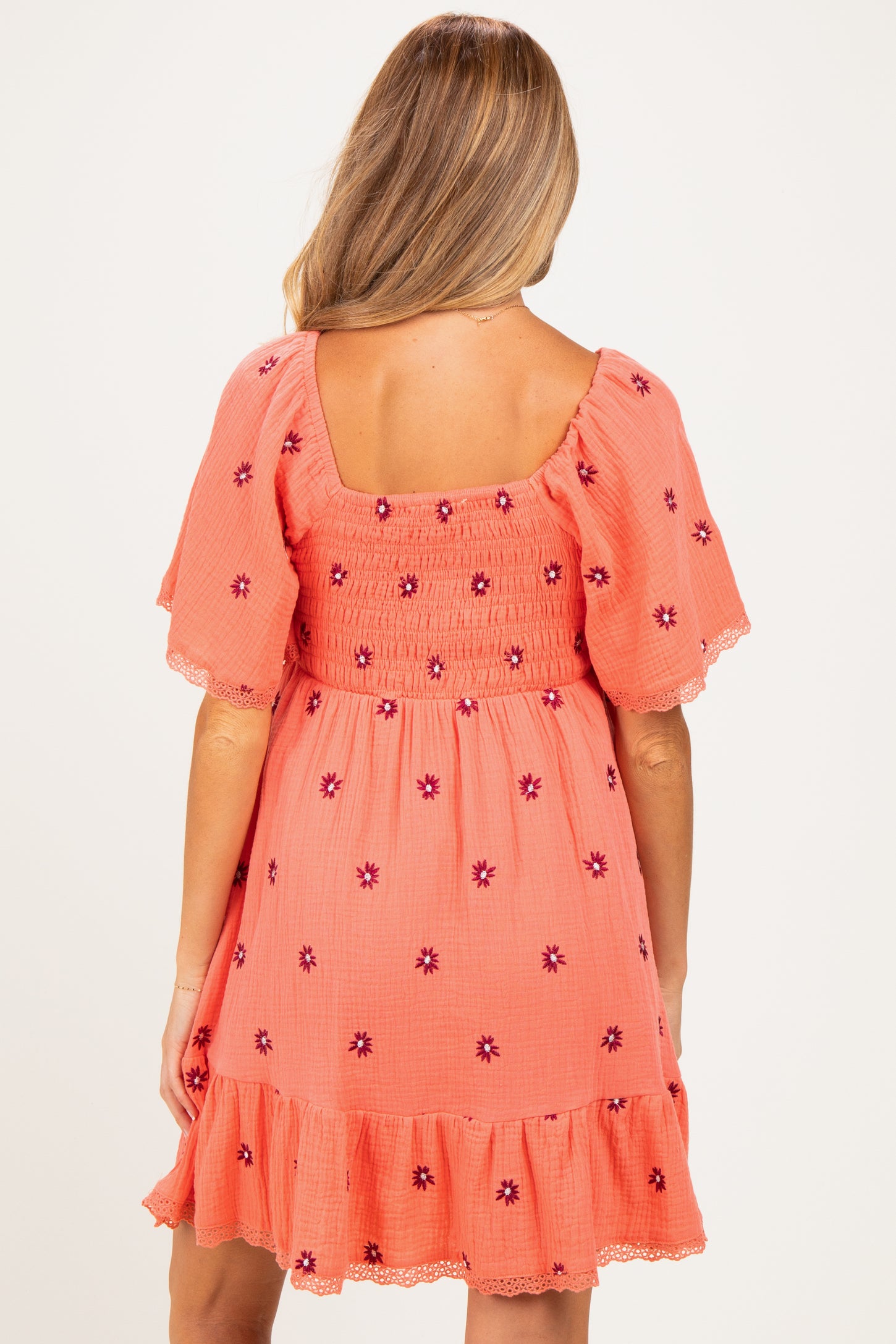 woman wearing a coral maternity dress with floral embroidery and short sleeves, showing a smocked back design