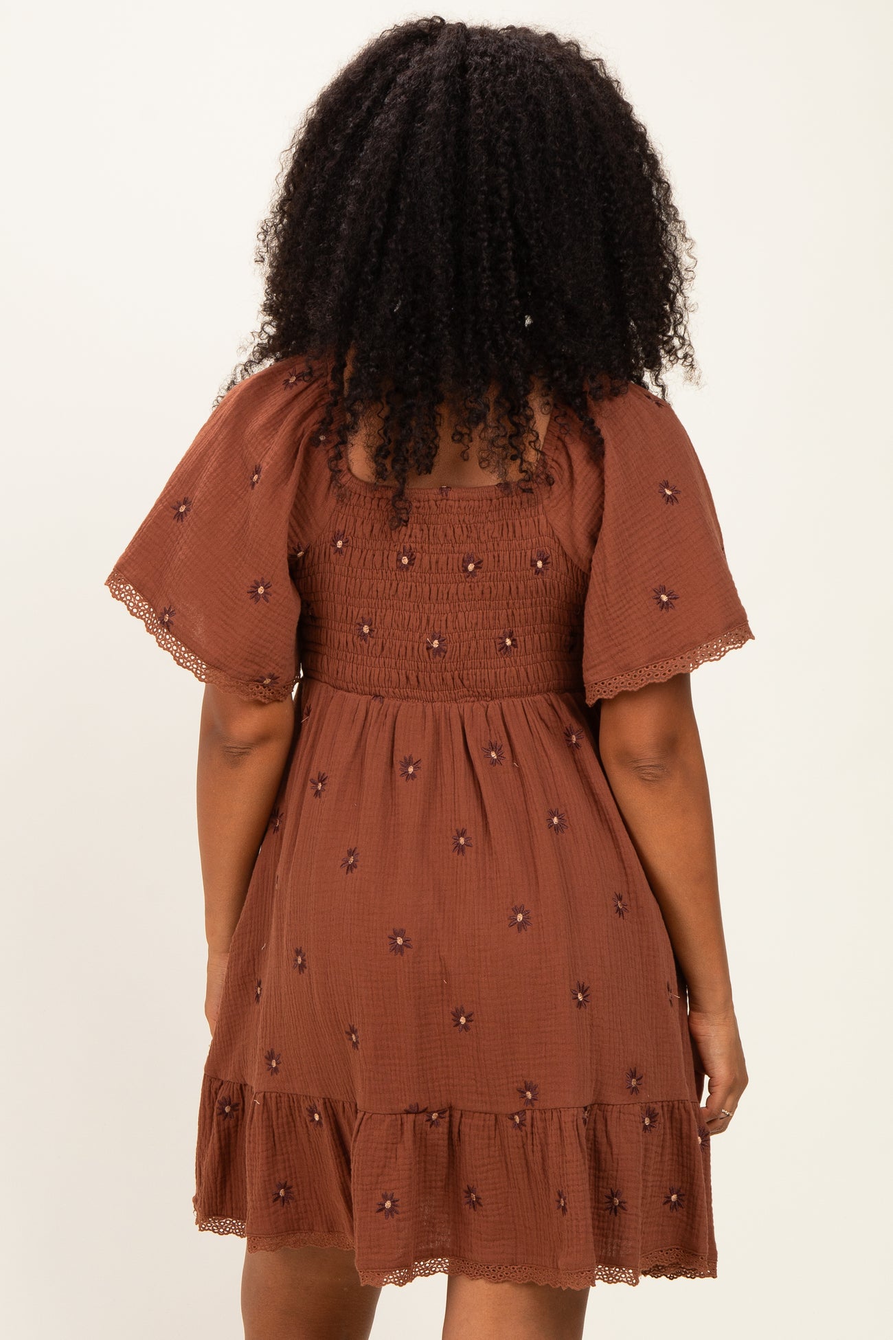 woman wearing a brown floral embroidered smocked dress with short sleeves and a ruffled hem