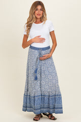 woman wearing a white short sleeve top and a blue patterned maternity maxi skirt, holding her baby bump