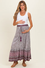 woman wearing a white tank top and a floral maternity maxi skirt, holding her baby bump