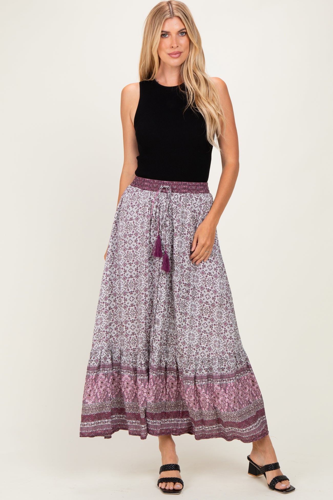 woman wearing a black sleeveless top and a long printed skirt with a tie waist and tassels