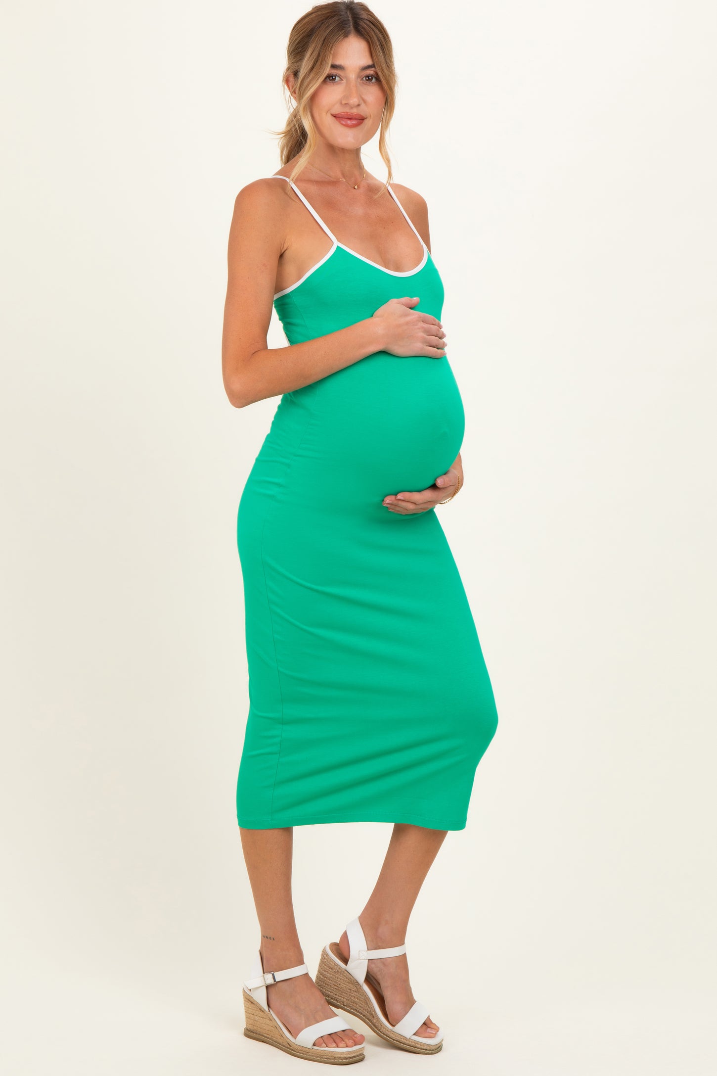 woman wearing a green maternity midi dress with white straps and holding her baby bump