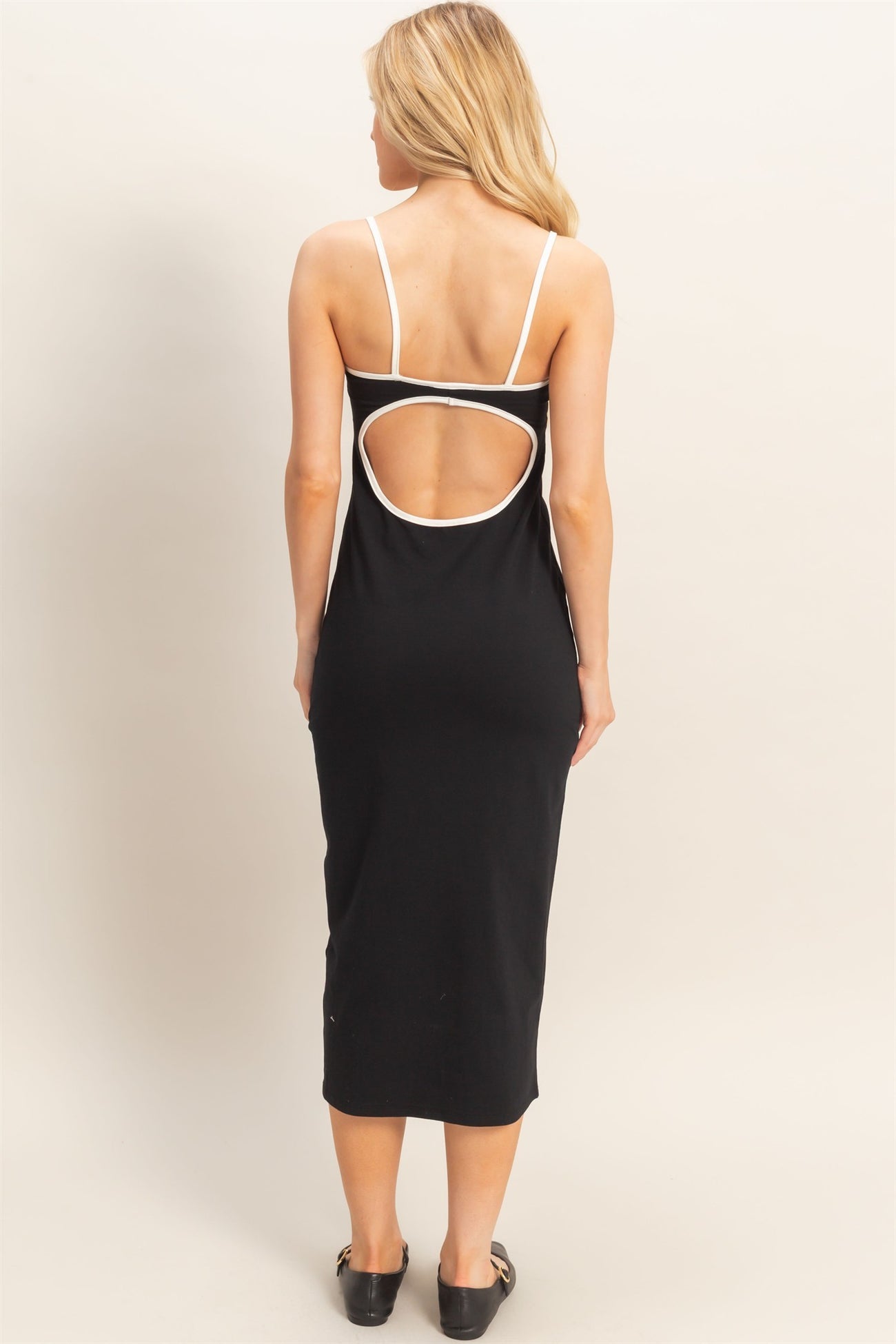woman wearing a black midi dress with a white trim and cutout detail at the back, styled with black shoes