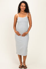woman wearing a light gray spaghetti strap maternity dress and holding her baby bump