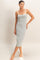 woman wearing a gray midi slip dress with thin white straps, standing barefoot against a light background