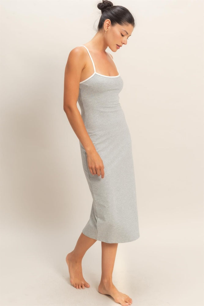 woman wearing a light gray midi slip dress with white straps, standing barefoot and slightly looking down