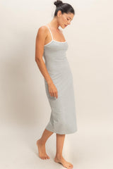 woman wearing a light gray midi slip dress with white straps, standing barefoot and slightly looking down