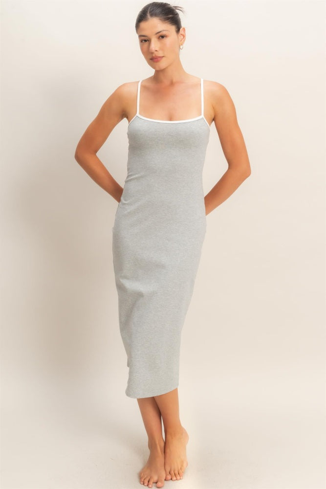 woman wearing a gray midi dress with thin white straps, standing barefoot and posing with hands on her hips