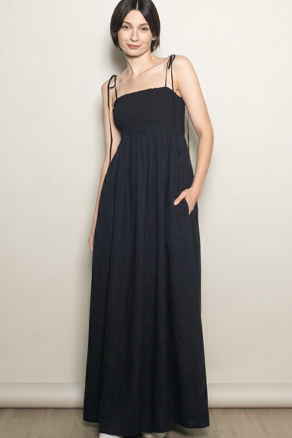woman wearing a black smocked maxi dress with adjustable straps and side pockets