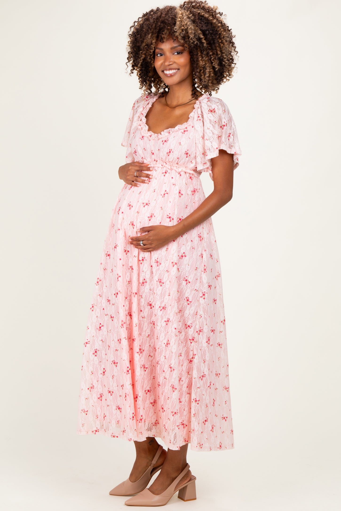 woman wearing a pink floral maternity dress with short puff sleeves and holding her baby bump