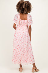 woman wearing a pink floral maternity maxi dress with short flutter sleeves and a flowing silhouette, showing off a baby bump