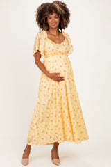 woman wearing a yellow floral maternity maxi dress and holding her baby bump