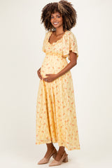 woman wearing a yellow floral maternity dress with short sleeves and holding her baby bump