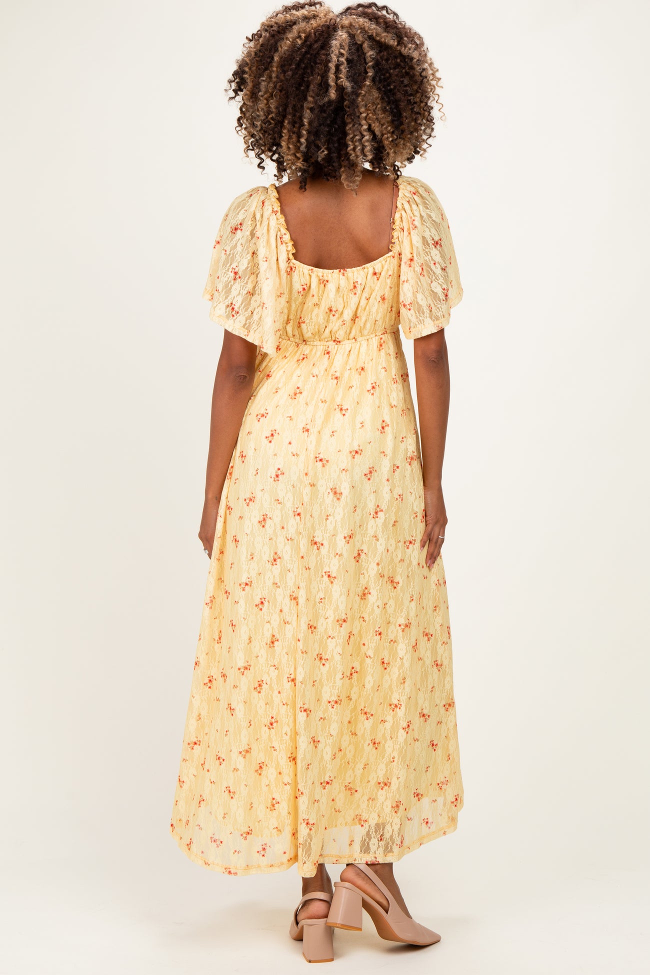 woman wearing a yellow floral maternity dress with flutter sleeves and a flowing skirt, showing a baby bump from behind