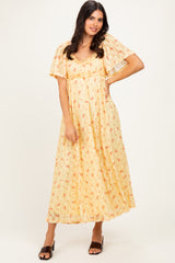 woman wearing a yellow floral maxi dress with flutter sleeves and a layered design, standing against a neutral background
