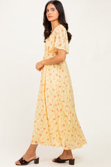 woman wearing a yellow floral maxi dress with short sleeves and a cinched waist, standing in profile