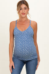 woman wearing a blue maternity tank top with a white floral print and showing her baby bump while smiling