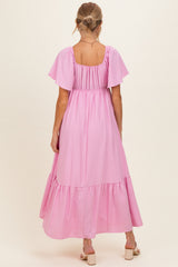 woman wearing a light pink maternity maxi dress with flutter sleeves and a tiered skirt, showing her baby bump from the back