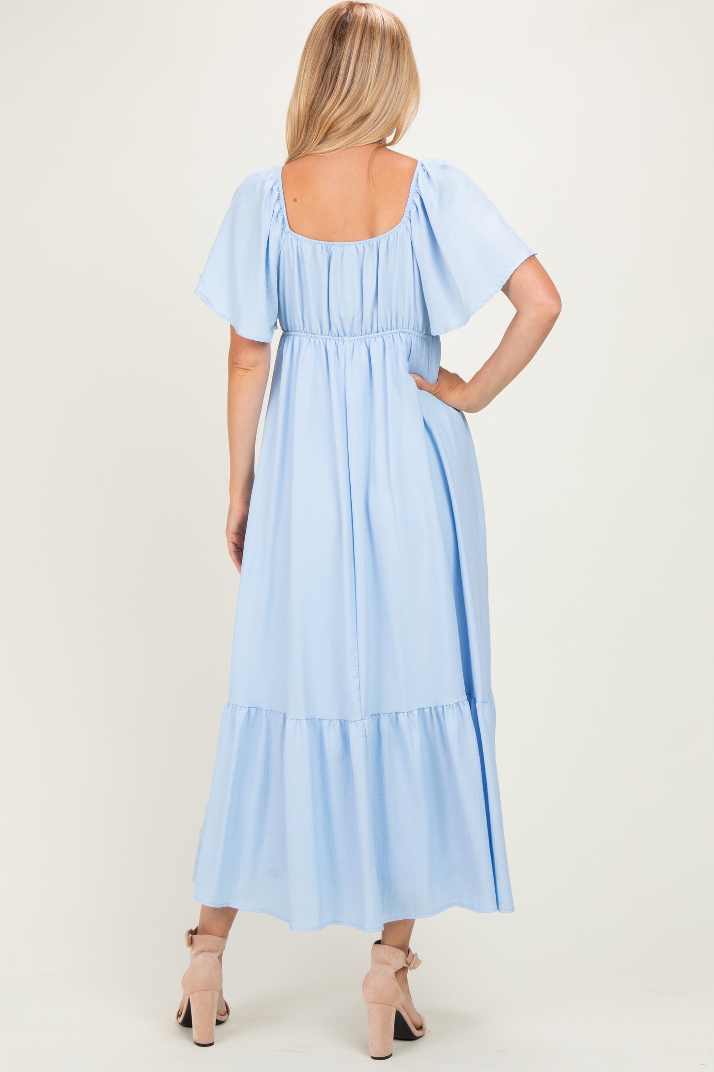woman wearing a light blue maxi dress with short flutter sleeves and a tiered skirt, viewed from the back