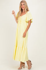 woman wearing a yellow maxi dress with flutter sleeves and a tie front detail, paired with beige heels