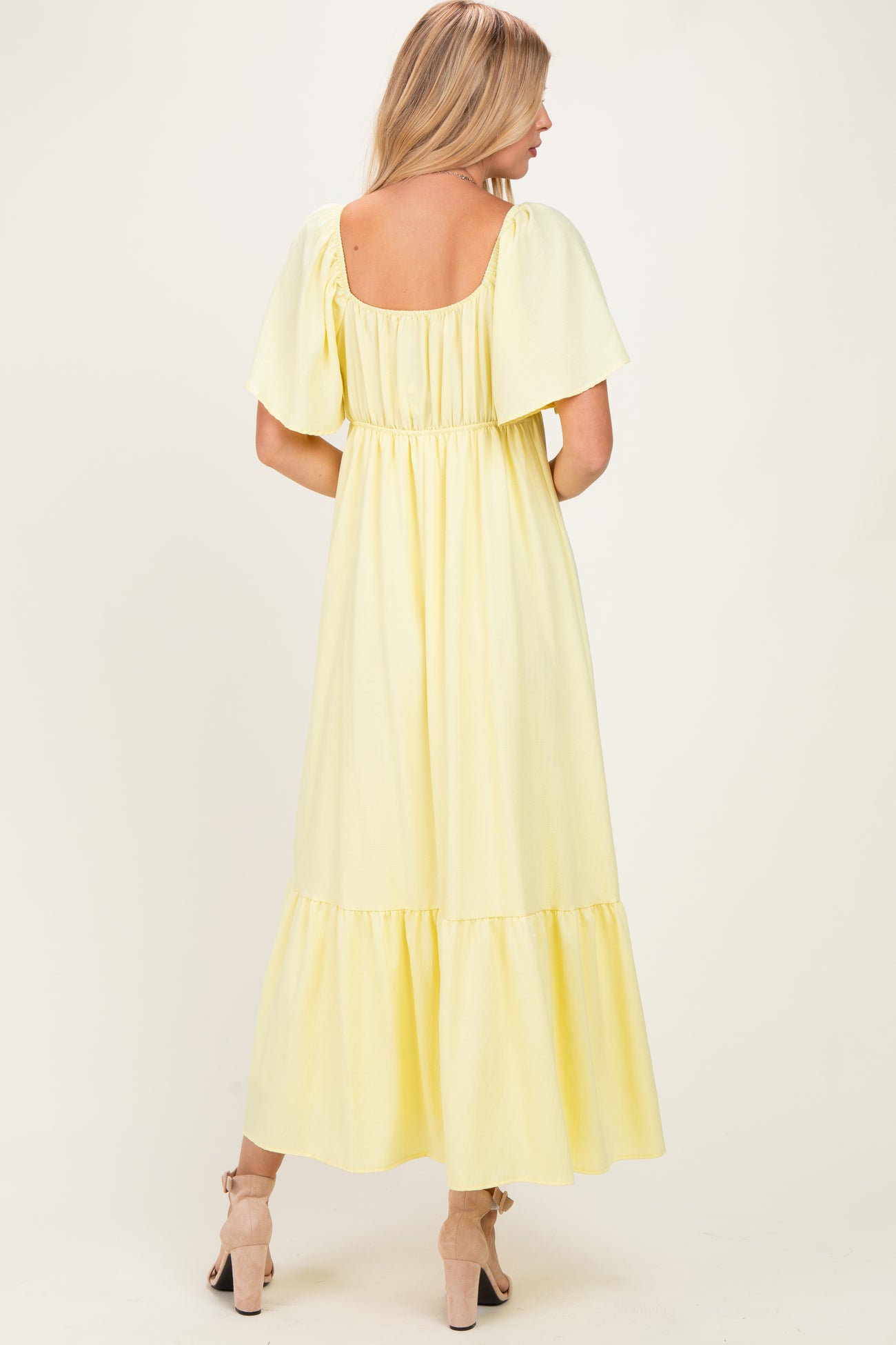 woman wearing a yellow maxi dress with short sleeves and a tiered hem, seen from the back