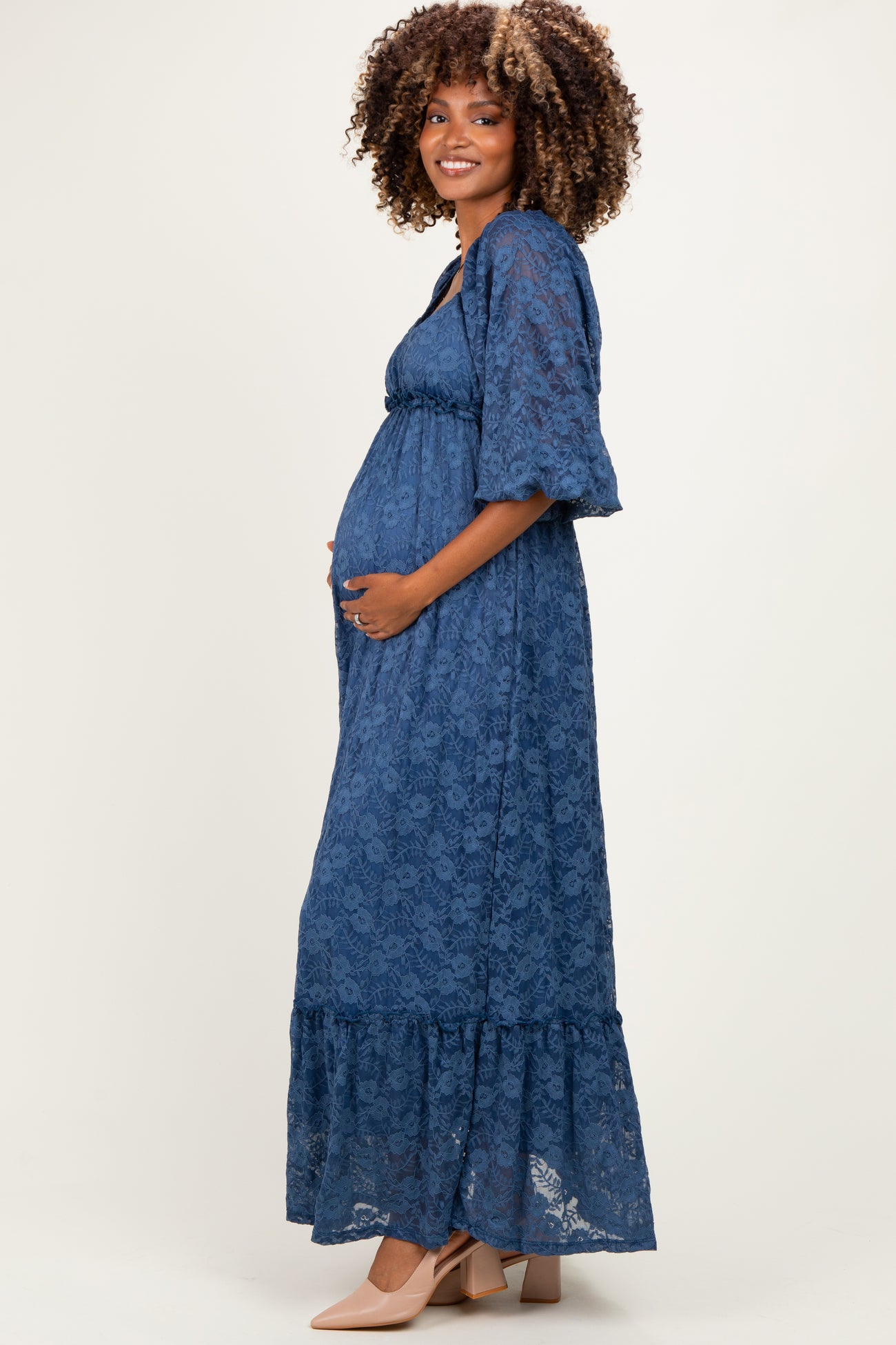 woman wearing a navy blue lace maxi maternity dress with a ruffled hem and holding her baby bump