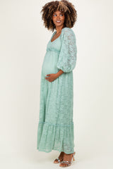 woman wearing a long mint green lace maternity dress with puff sleeves and a fitted bodice, showing her baby bump