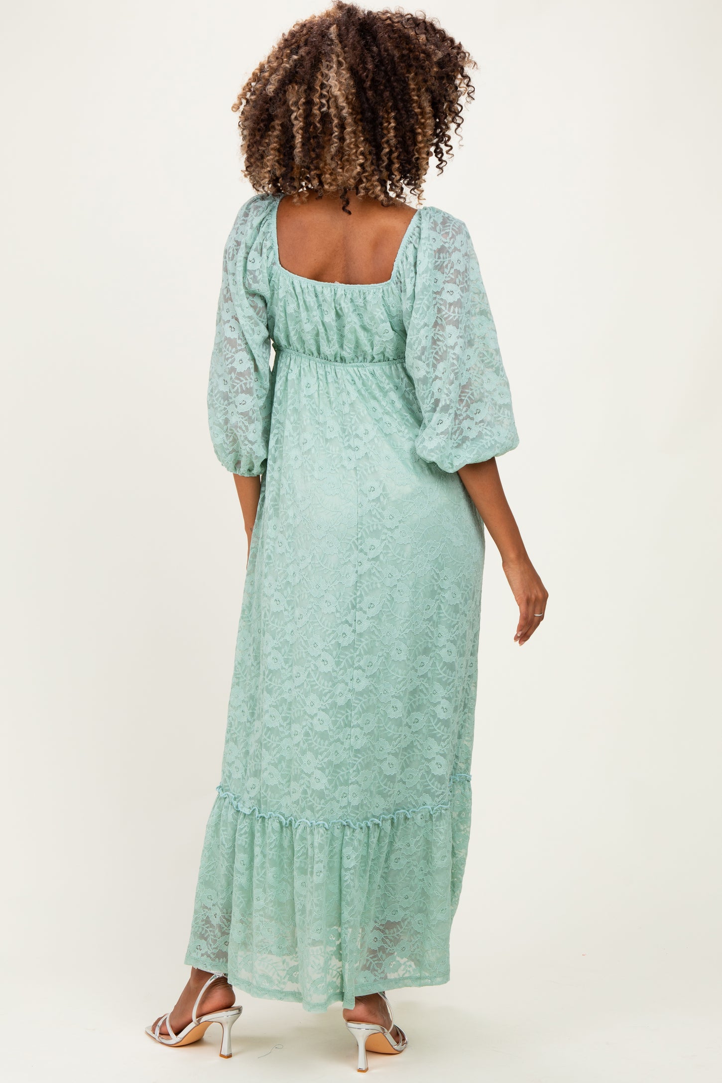 woman wearing a mint green lace maternity maxi dress with puff sleeves and a tiered hem, showing off her baby bump