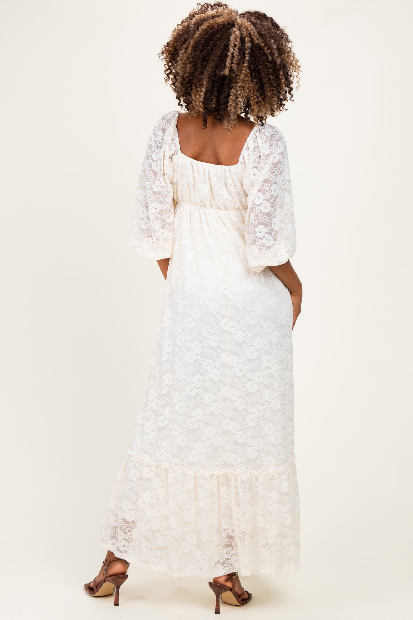 woman wearing a cream lace maternity maxi dress with puff sleeves and a tiered hem, showing off a baby bump