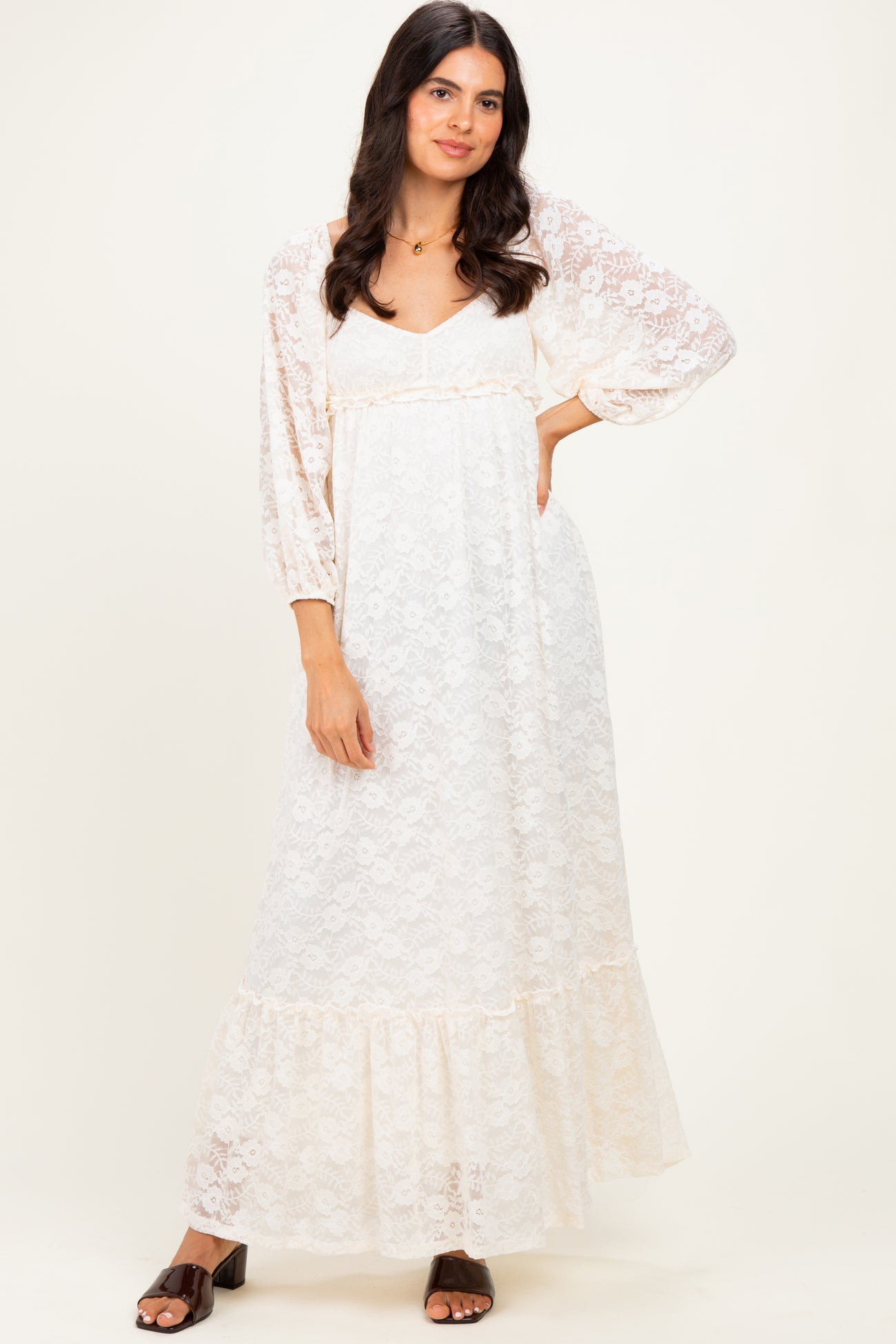 woman wearing a white lace maxi dress with long sleeves and a ruffled hem, standing against a light background