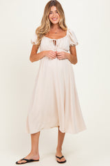 woman wearing a light beige puff sleeve maternity dress with a drawstring neckline and a flowing skirt, revealing a baby bump
