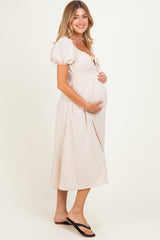 woman wearing a beige maternity dress with puff sleeves and smocked waist, holding her baby bump