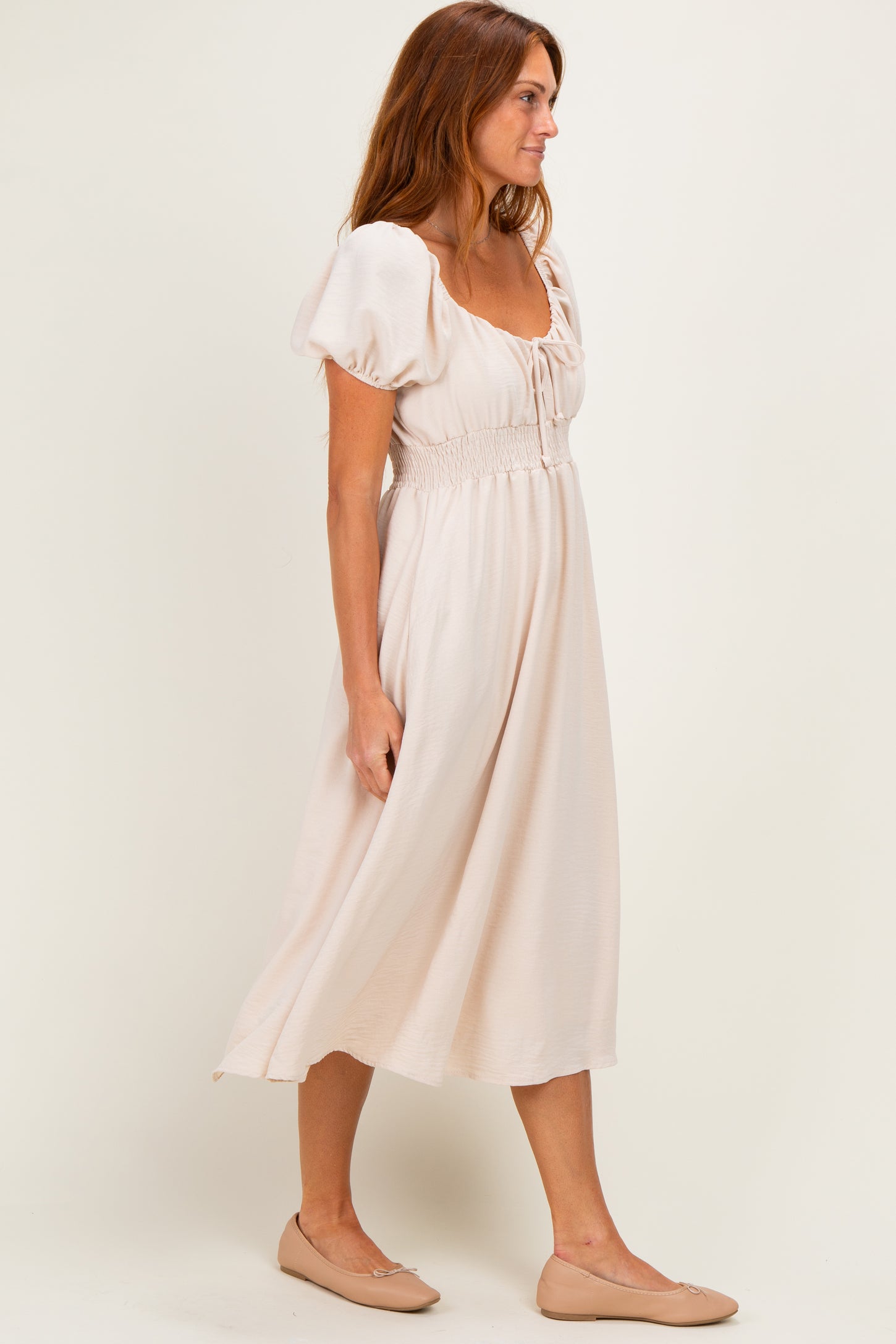 woman wearing a light pink midi dress with puff sleeves and smocked waist, paired with nude ballet flats