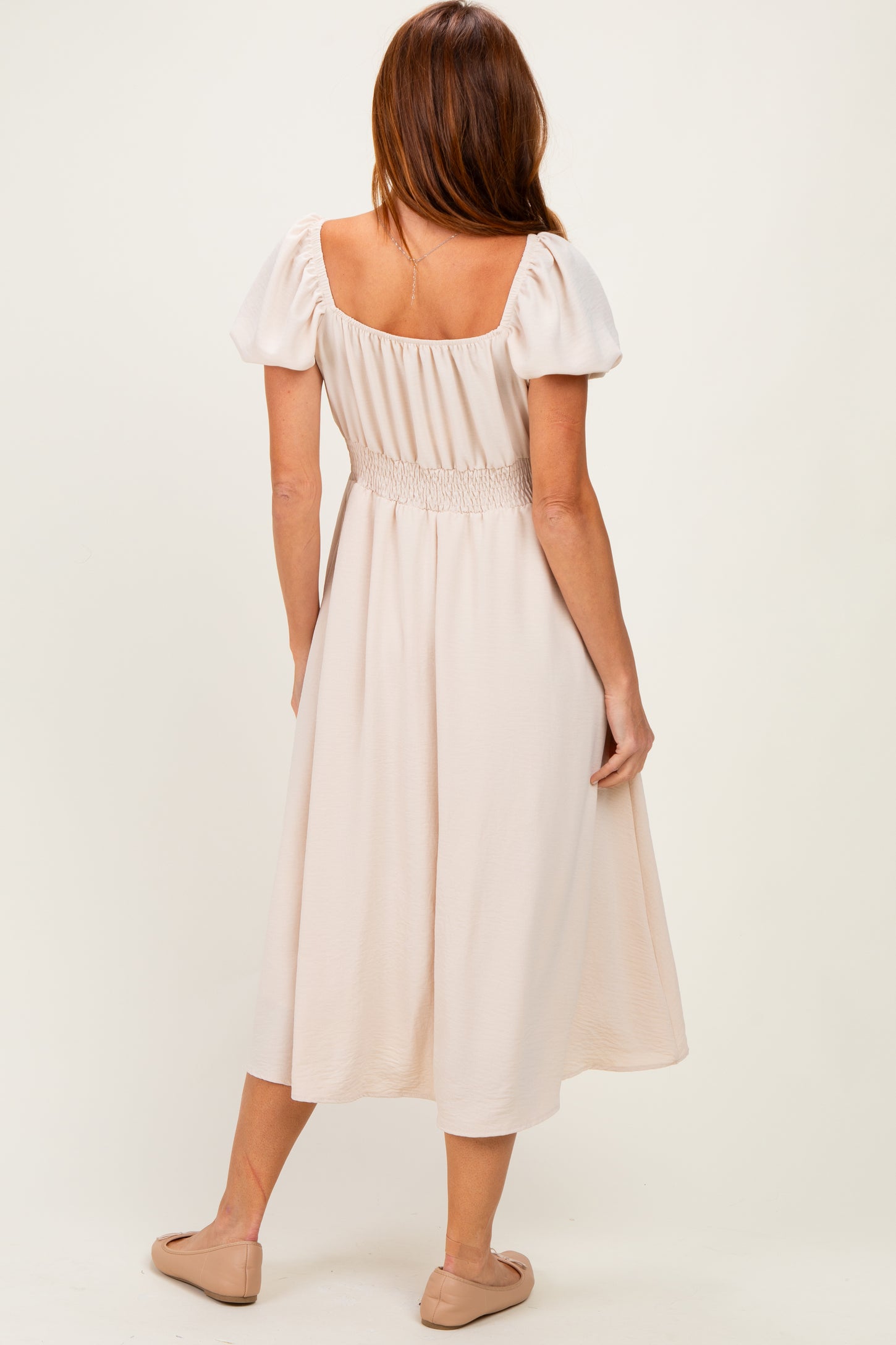 woman wearing a light pink mid-length dress with puff sleeves and smocked bodice, shown from the back