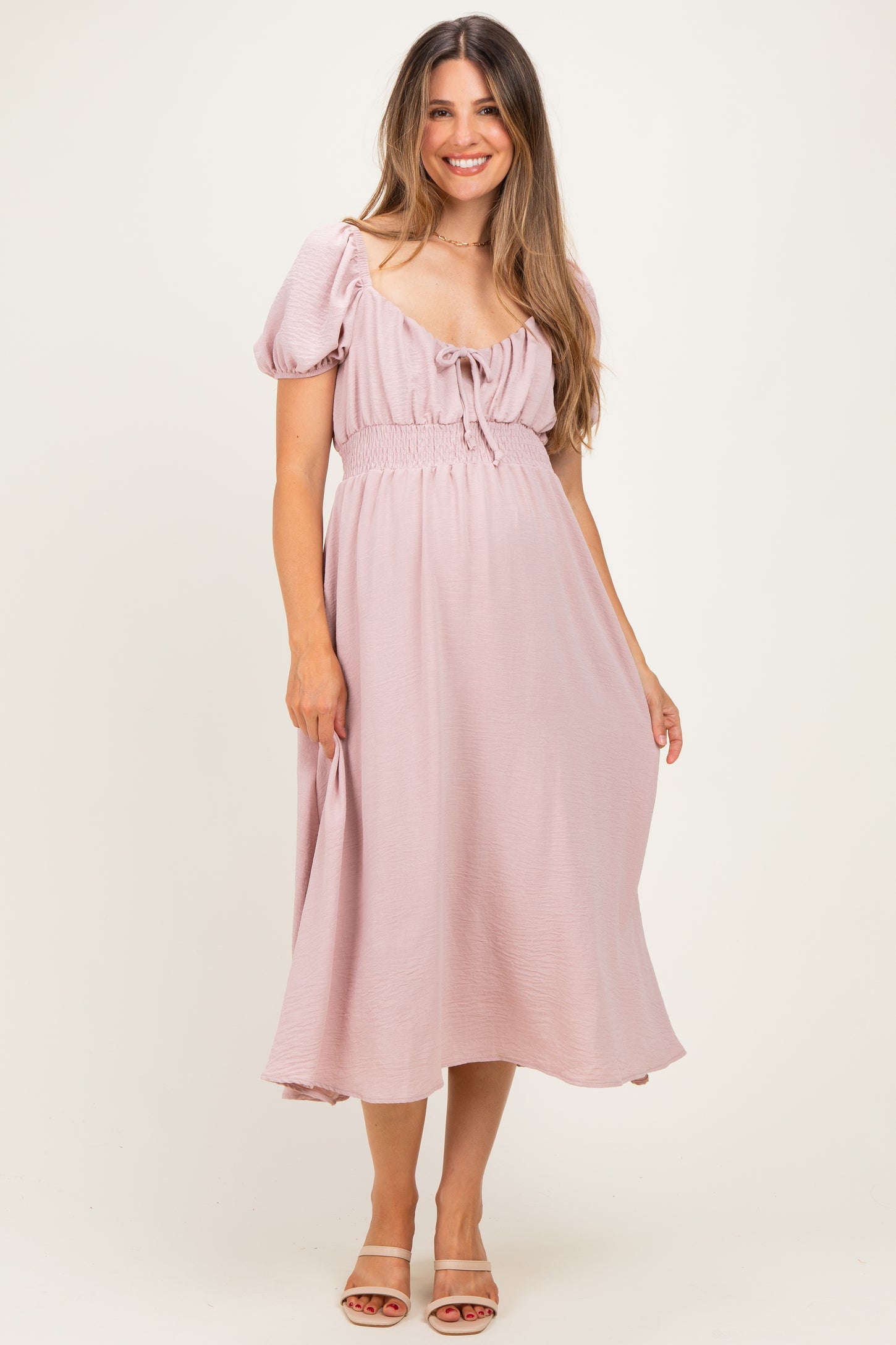 woman wearing a light pink maternity dress with puff sleeves and a tie-front detail, standing with a baby bump visible