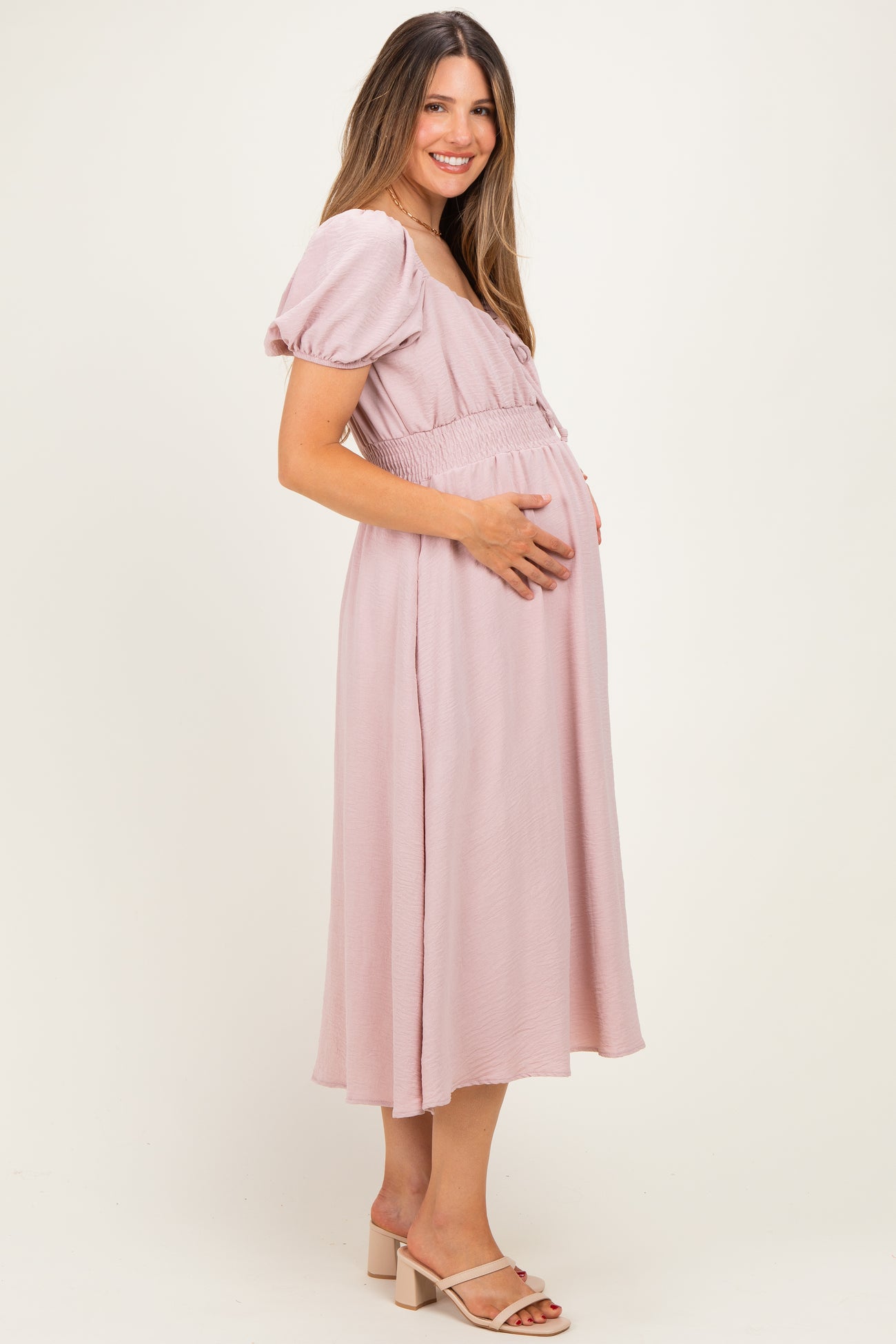 woman wearing a pink maternity dress with short puff sleeves and holding her baby bump