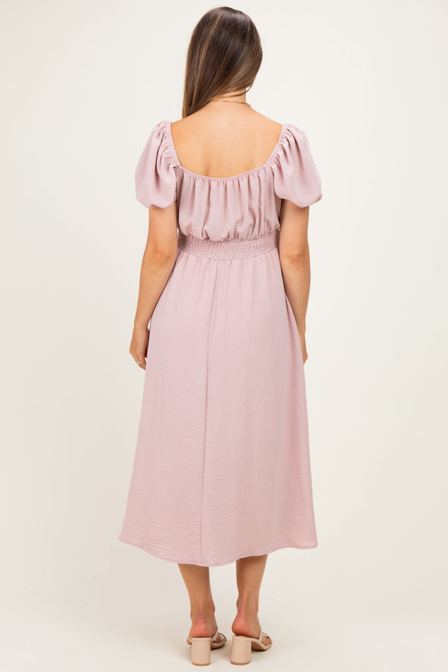 woman wearing a pink maternity dress with puff sleeves and a smocked waist, seen from the back