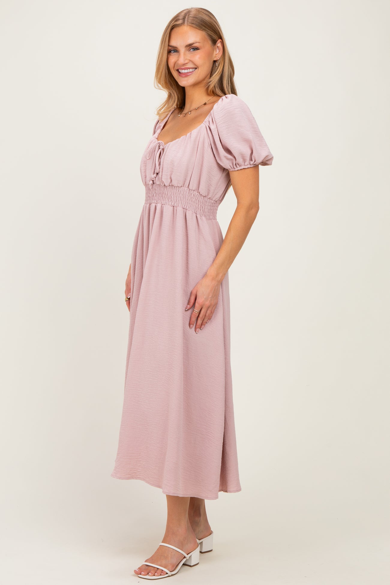 woman wearing a light pink midi dress with puff sleeves and a smocked bodice, posed in a side profile