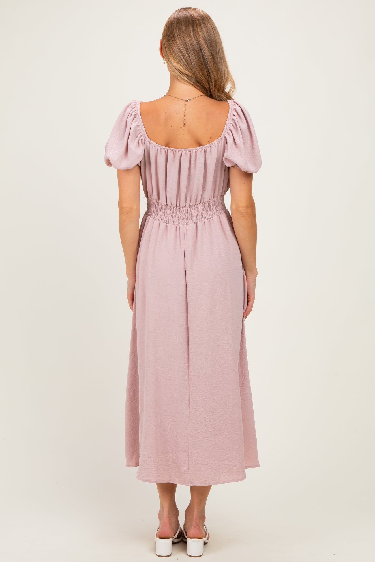 woman wearing a back view of a light pink maxi dress with puff sleeves and a smocked waist