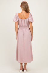 woman wearing a back view of a light pink maxi dress with puff sleeves and a smocked waist