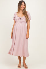 woman wearing a soft pink maternity dress with puff sleeves and a tie front detail, showcasing her baby bump