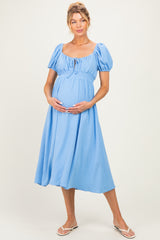 woman wearing a light blue maternity dress with puff sleeves and a smocked bodice, holding her baby bump