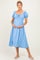 woman wearing a light blue maternity dress with puff sleeves and a smocked bodice, holding her baby bump