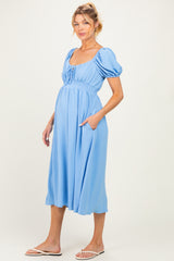 woman wearing a light blue maternity dress with puff sleeves and side pockets, showcasing her baby bump