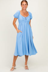 woman wearing a blue midi dress with puff sleeves and pockets, standing and smiling